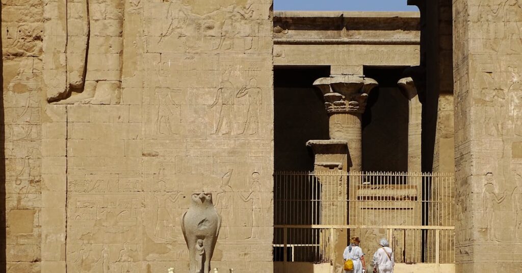 Sunlit façade of an ancient Egyptian temple featuring intricate hieroglyphs and sculptures.